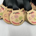 A close-up of several wooden medals on black ribbons. The medals are inscribed with “Epilepsy Action memory walk” and feature colorful footprints.