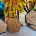 A collection of hexagonal wooden medals with colorful ribbons. The medals are engraved with Hampshire School Games and phrases like Determination and Team Work. The ribbons are blue, yellow, and green.