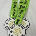 Three white medals with green ribbons that read Way of the Roses 2025. The medals feature a white rose design and the text WAY OF THE ROSES, SEE YORK RUN YORK on a white background.