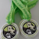 Two medals with green ribbons that read Helping Pets in Need. The medals feature cartoon images of a dog and a cat with the text, Cheltenham Animal Shelter – Ive made a difference today!.