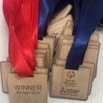 Wooden medals with red and blue ribbons are displayed. The medals are engraved with WINNER 9th April 2025, Special Olympics Great Britain logos, and Mitsubishi Electric branding.