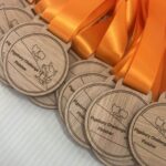 A group of wooden medals with orange ribbons, each engraved with “Figsbury Challenge Finisher” and an image of a fox holding a flag, displayed on a white surface.