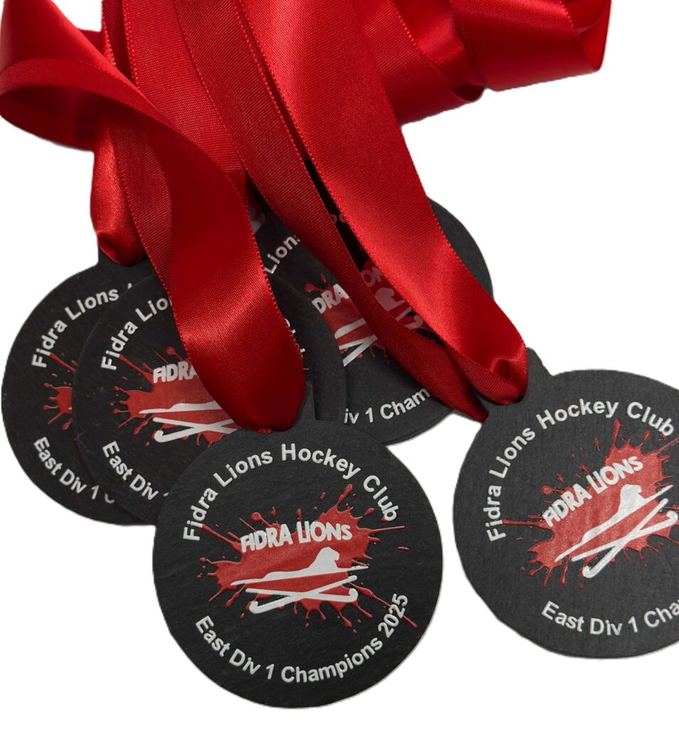 Four black Eco Medals with bright red ribbons are displayed. The medals read Fidra Lions Hockey Club East Div 1 Champions 2015 with a lion paw print and a hockey stick graphic in the centre.