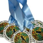 Four round medals with light blue ribbons, featuring colourful illustrations of flowers and birds, labelled Regents Park 2024 Mini Magpie Trail..