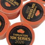 Stacks of orange medals with Thruxton 10K Series 2026 and a racing car icon printed on them, along with event dates and Thruxton Motor Racing Circuit in smaller text around the edges.
