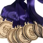 A row of wooden medals with purple ribbons, engraved with FUN RUN TOGETHER and I'M A WINNER along with a group running graphic.