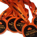 A group of orange medals with Thruxton 10K Series 2026 printed on them, attached to matching orange ribbons.