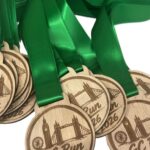 Several wooden medals with green ribbons, engraved with GC Run 2026 and London landmarks, are stacked together.