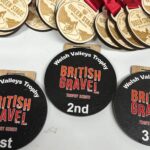 A group of wooden medals with red ribbons reads Queen Stage. In front, three black round awards display Welsh Valleys Trophy British Gravel Trophy Series for 1st, 2nd, and 3rd places.
