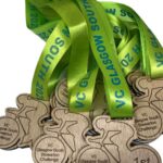 A pile of wooden medals with bright green ribbons, labelled VC Glasgow South Stewarton Challenge, with one medal showing 1st..