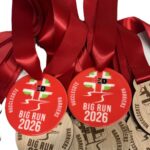 A collection of Big Run 2026 medals with red ribbons, featuring both colourful and wooden designs, labelled Hucclecote Harriers..