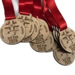 Wooden medals with red ribbons, engraved with Big Run 2026, a runner graphic, and Hambleton & Ridgecott. The medals are arranged in an overlapping row on a white background.