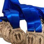 A group of wooden medals with blue ribbons labelled J&M RUNNING 5K FINISHER, featuring silhouettes of runners engraved on each medal.