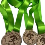 Wooden medals with green ribbons, engraved with Rebecca's 60th Birthday, June 2026, and an image of a tree, arranged overlapping on a white background.