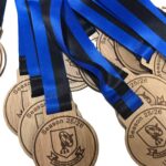 A pile of wooden medals with blue and black ribbons, labelled Season 25/26, Under 8s and featuring a sports club logo.