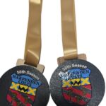 Two gold medals with tan ribbons display the Harpenden Colts F.C. crest. Both read 50th Season above and 2025 - 2026 below the crest.