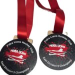Two round black medals with red ribbons. The medals read FIDRA LIONS, with a red lion logo, and Fidra Lions Hockey Club East Division 5 Champions in white letters around the edge.