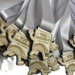 Wooden medals with white ribbons, featuring a book design that reads YOU SMASHED IT 1 MILE FINISHER and a smiling star, overlapping in a pile.