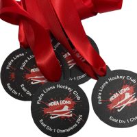 Four black Eco Medals with bright red ribbons are displayed. The medals read Fidra Lions Hockey Club East Div 1 Champions 2015 with a lion paw print and a hockey stick graphic in the centre.