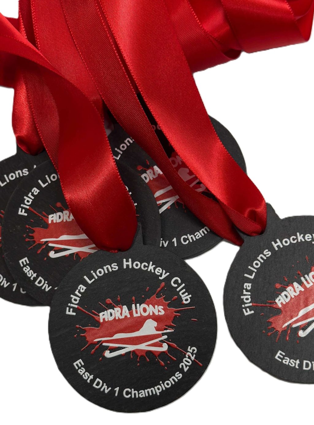 Four black Eco Medals with bright red ribbons are displayed. The medals read Fidra Lions Hockey Club East Div 1 Champions 2015 with a lion paw print and a hockey stick graphic in the centre.